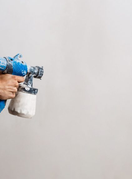 Worker painting wall with spray gun in white color. Copy space.
